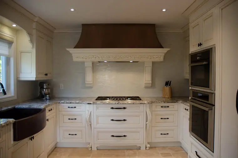 A finished cream kitchen with a custom range hood and copper sink