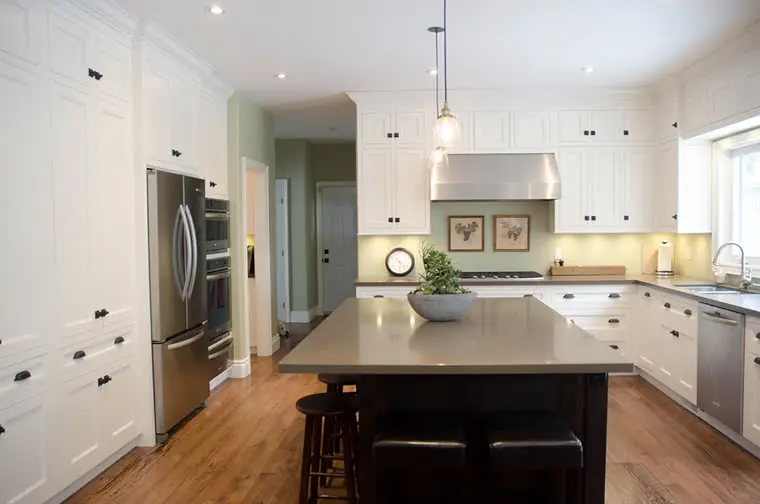 A white custom kitchen with a dark island, seen from the doorway